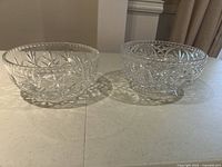 Two clear glass bowls placed side by side on a white surface showing overall shape and pattern details.