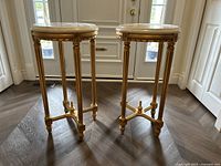 Front view of both gold-finish metal end tables with round marble tops against a door