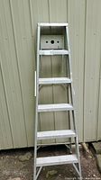 Front view of the 6ft aluminum step ladder showing six steps and the top platform against a corrugated metal wall.