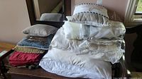 Stack of queen size bedding and throw pillows arranged on a wooden table for display