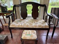Front view of wood framed two-seat bench with decorative backrest and patterned beige upholstery. Matching footstool visible in front.