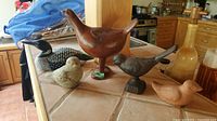 Overview of five bird figurines on tiled kitchen counter, showing size and varied materials.