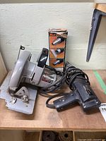 Black & Decker 7.25 inch circular saw and electric paint remover placed on a table, cords visible, nozzle attachments in box.