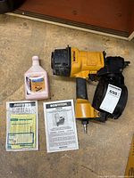Top-down view of Bostitch coil-fed pneumatic nailer with pink lubricant bottle and two manuals on workbench