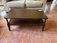Front view of the dark wood coffee table with visible bottom shelf and four legs, placed on tile floor in front of a beige couch.