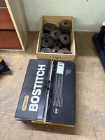 Two boxes of coil nails, one Stanley Bostitch branded box and one plain crate containing coiled nails, placed on workshop floor