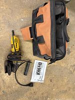 Angle grinder, side handle, grinding wheel, manual and tool bag shown on floor, viewed from above.