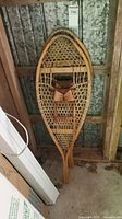 Single vintage wooden snowshoe leaning showing full profile and traditional design