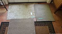 Three entrance mats placed on tiled floor: one floral pattern beige mat, two braided natural fiber mats.