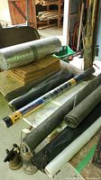 Image showing garden screening rolls, silver reflective insulating roll, and stack of brown leaf bags on a table in a garage/workshop space.
