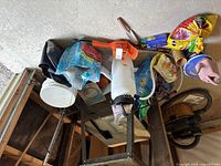 View of all gardening items arranged on a table and floor including the hedge trimmer, garden sprayer, gloves, and seed bags.