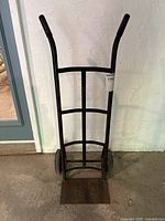 Front view of the black two-wheeled hand truck showing the curved handles with rubber grips, vertical and horizontal frame supports, and flat loading platform.