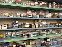 Wide view of three shelves showing many jars and plastic containers of screws and hardware items.