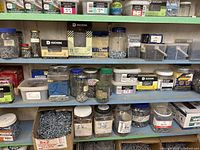 Full view of three shelves filled with various hardware including nails, screws in jars and boxes.