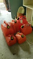Photo showing six red plastic jerry cans arranged on a floor, various sizes visible, black spouts with yellow caps on each.