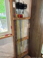 View of two large black bristle chimney brushes and multiple yellow poles with red adjustment knobs mounted on wooden frame.