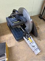 Side angle photo showing saw setup with blade guard, base, handle, and extra disk attached to the side.