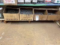 Four open cardboard boxes of various sizes of nails placed on a shelf.