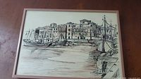 Framed original ink harbor drawing showing boats and buildings, artist signature visible but unclear.