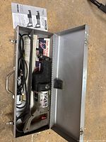 Porter Cable Tiger Saw Model 737 inside opened metal carry case with cords, extra blades and manuals