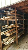 Wood planks and pieces stored on a multi-tier wooden rack inside a wooden structure.