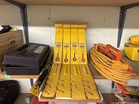 Photo showing four yellow Roofers World Endura roofing brackets alongside black drill bit cases and an orange extension cord