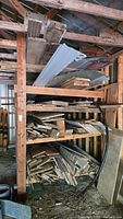 Variety of wood and metal scrap stored on a wooden shelving unit including beams, plank, and corrugated metal sheets