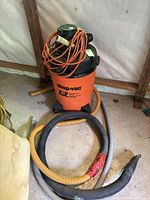 Orange Shop-Vac 13 gallon wet/dry vacuum on wheels with hoses and power cord coiled on top.