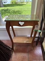 Photo of wood side table featuring a clear glass top, heart-shaped detail on front apron, curved legs, and a lower wooden shelf.
