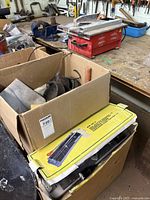 Overview photo of cardboard boxes with tile saw tools, hand cutters, and trowels visible.