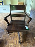 Front view of vintage wooden swivel office chair showing wide seat, curved armrests, and caster wheels.