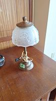 Full view of the vintage accent lamp on a wooden surface showing the frosted glass floral shade and brass base.