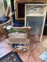 Vintage Economy washboard, manual wooden clothes wringer (Model GH), and basket with wooden clothes pins arranged on floor.
