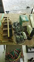 Top view of assorted items on wooden table including rusted tire traction aid with black bristles and wooden handle, two green walkie talkies, analog thermometer in box, phone handset, black flashlight, and multicolored cables.