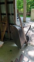 Side view of the vintage wheelbarrow showing metal tray, wooden handles, metal frame, and one black rubber tire.
