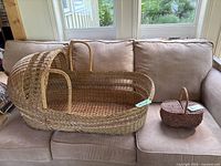 Wicker bassinet with rounded canopy and small basket on couch.
