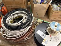 Bundle of various electrical wires coiled and mixed in a pile with some other spools nearby
