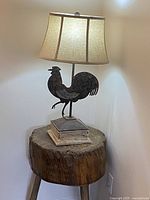 Table lamp lit on, showing the rooster metal base on stacked book-style pedestal and fabric shade