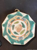 Front view of an octagonal porcelain pendant with a multicolored floral pattern and a silver metal rim.