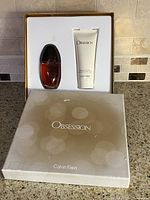 Calvin Klein Obsession gift set in original beige box with plastic insert holding Eau de Parfum spray bottle and body lotion tube.