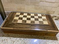 Closed wooden chess and checkers board with walnut or mahogany wood finish and inlaid checkered pattern.
