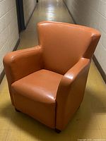 Front view of orange leather armchair with wooden legs on yellow floor in a hallway.