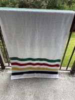 Front view of large white towel with green, red, yellow, and blue horizontal stripes near one end draped over balcony railing.