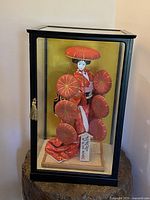 Full view of the Geisha doll inside black wooden frame glass display case with gold tassel