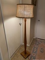 Unlit floor lamp showing straight-on view highlighting teak wood base and burlap shade.