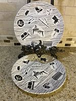 Two plates with black and white mid-century modern illustration pattern displayed standing and lying down on tabletop.