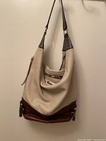 Full side view of beige and brown leather shoulder bag hanging, showing overall shape, color contrast, and strap details.
