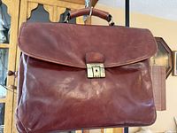 Front view of the vintage brown leather Bugatti briefcase showing smooth leather surface and centered brass-tone buckle clasp closure.