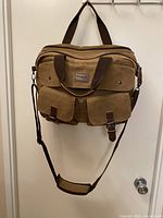 Front view of brown canvas messenger bag showing dual front flap pockets with buckles, main compartment zipper, and attached handles.