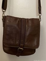 Front view of vintage brown leather shoulder bag showing flap, buckle detail, and adjustable strap attachments.